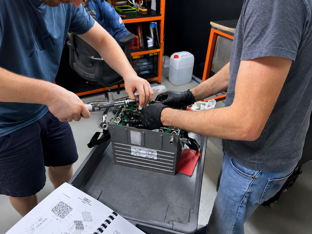 Two technicians using a torque wrench on an opened aircraft Ni-Cd battery, working from a maintenance manual